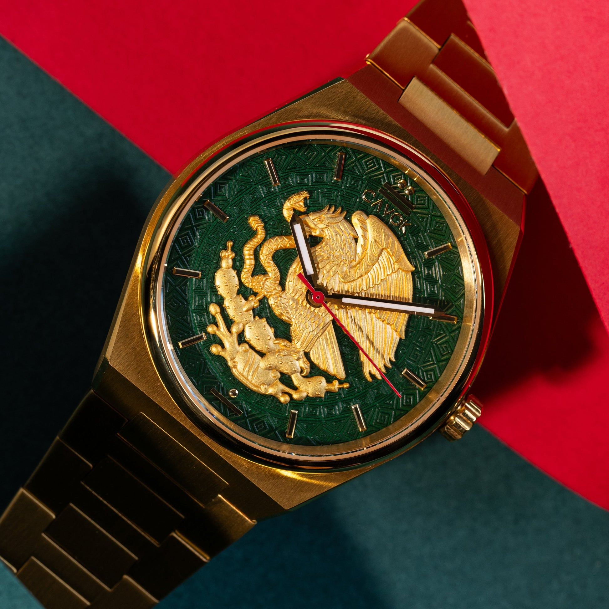 Gold watch with green face and eagle emblem on a red and blue background. Mexican Eagle