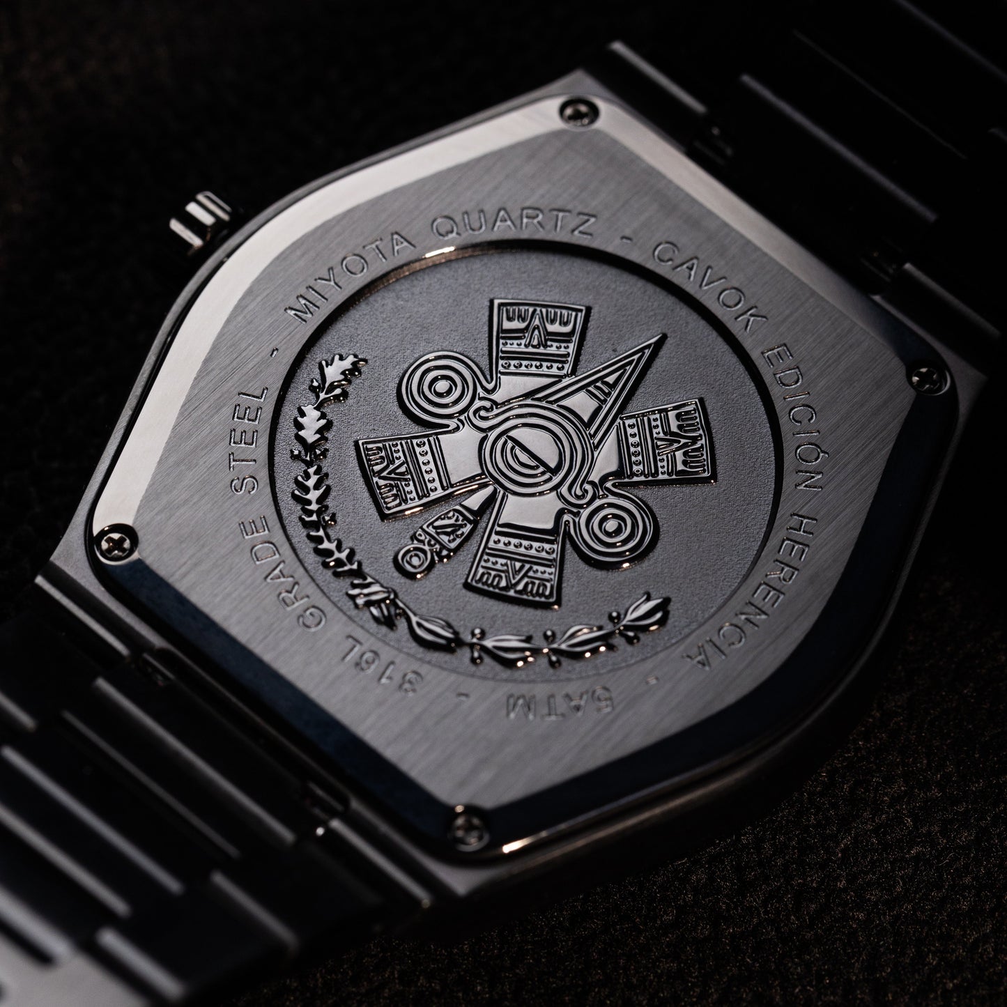 Close-up of a watch case with Ollin symbol engraved design on a dark background