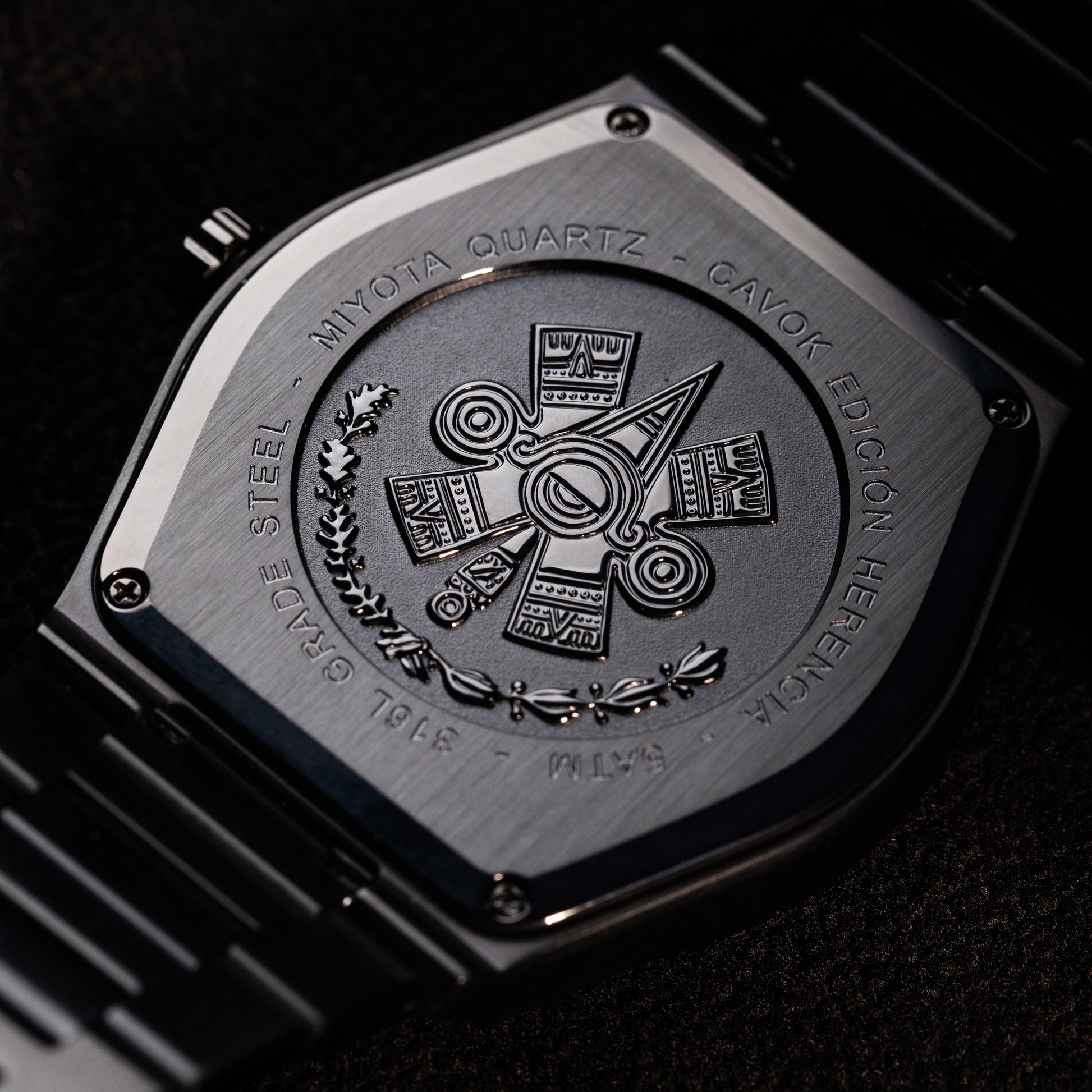 Close-up of a watch case with Ollin symbol engraved design on a dark background